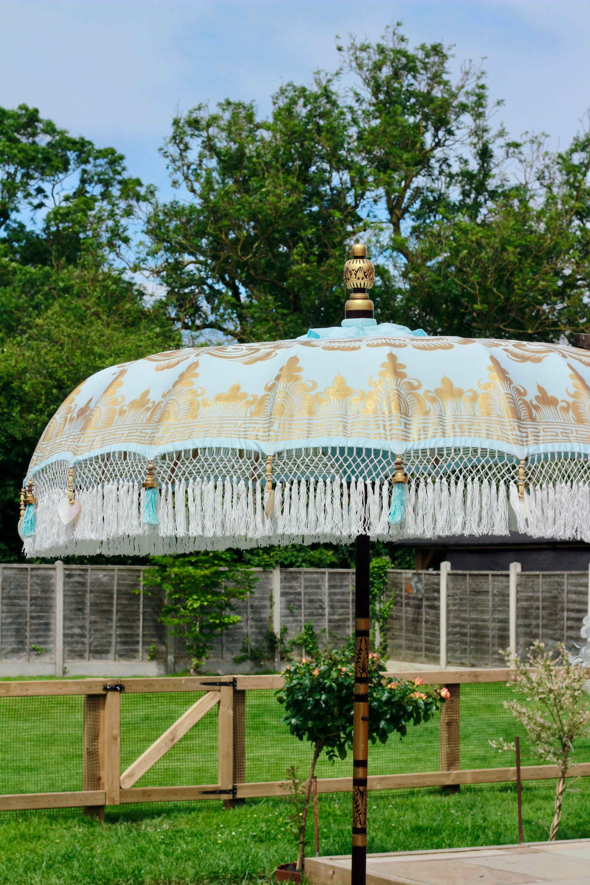 Close-up of white tassel fringe and mother of pearl shell heart detail on blue garden parasol