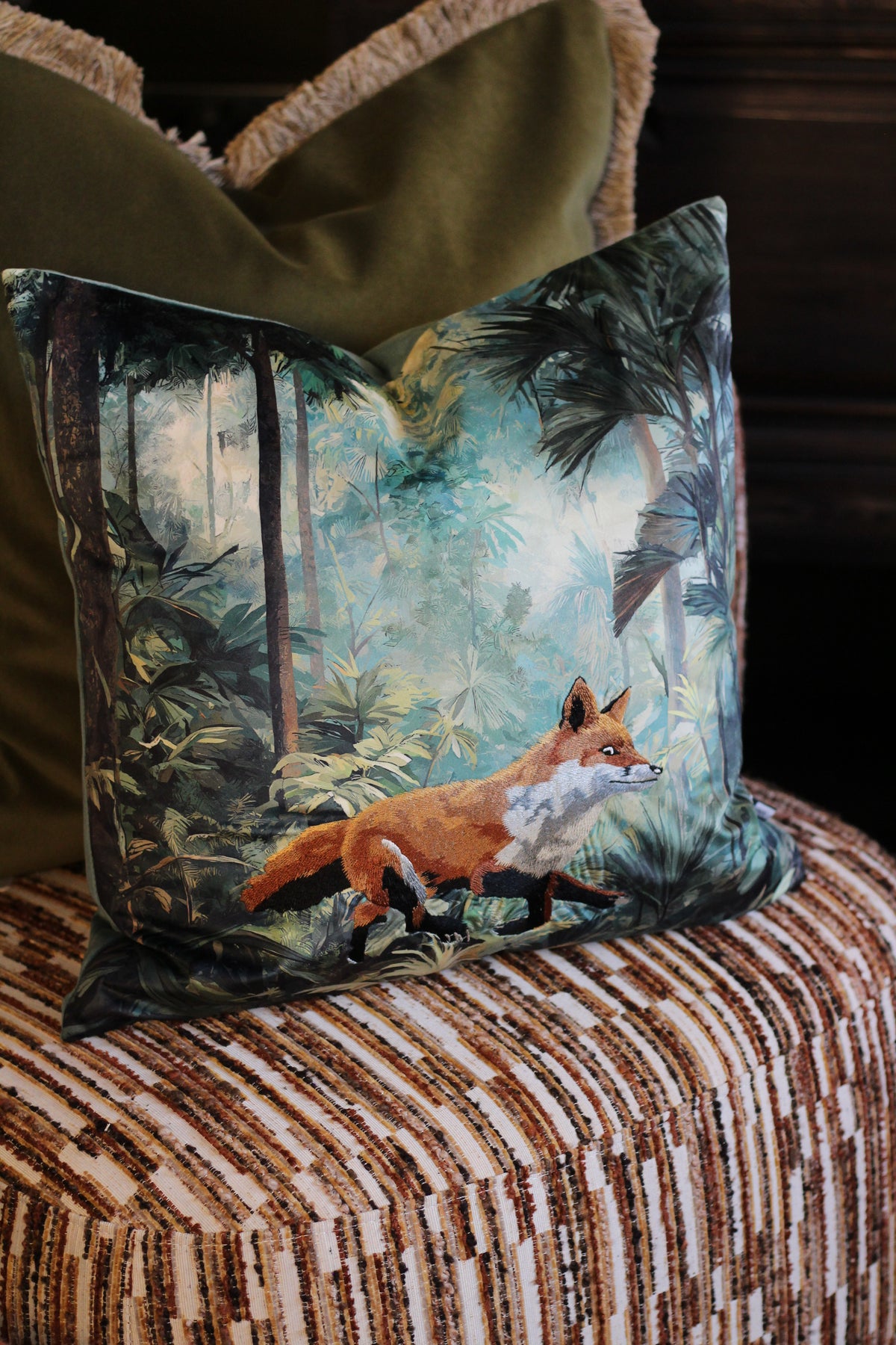 Bracken fox cushion styled with olive green velvet cushions on a striped armchair